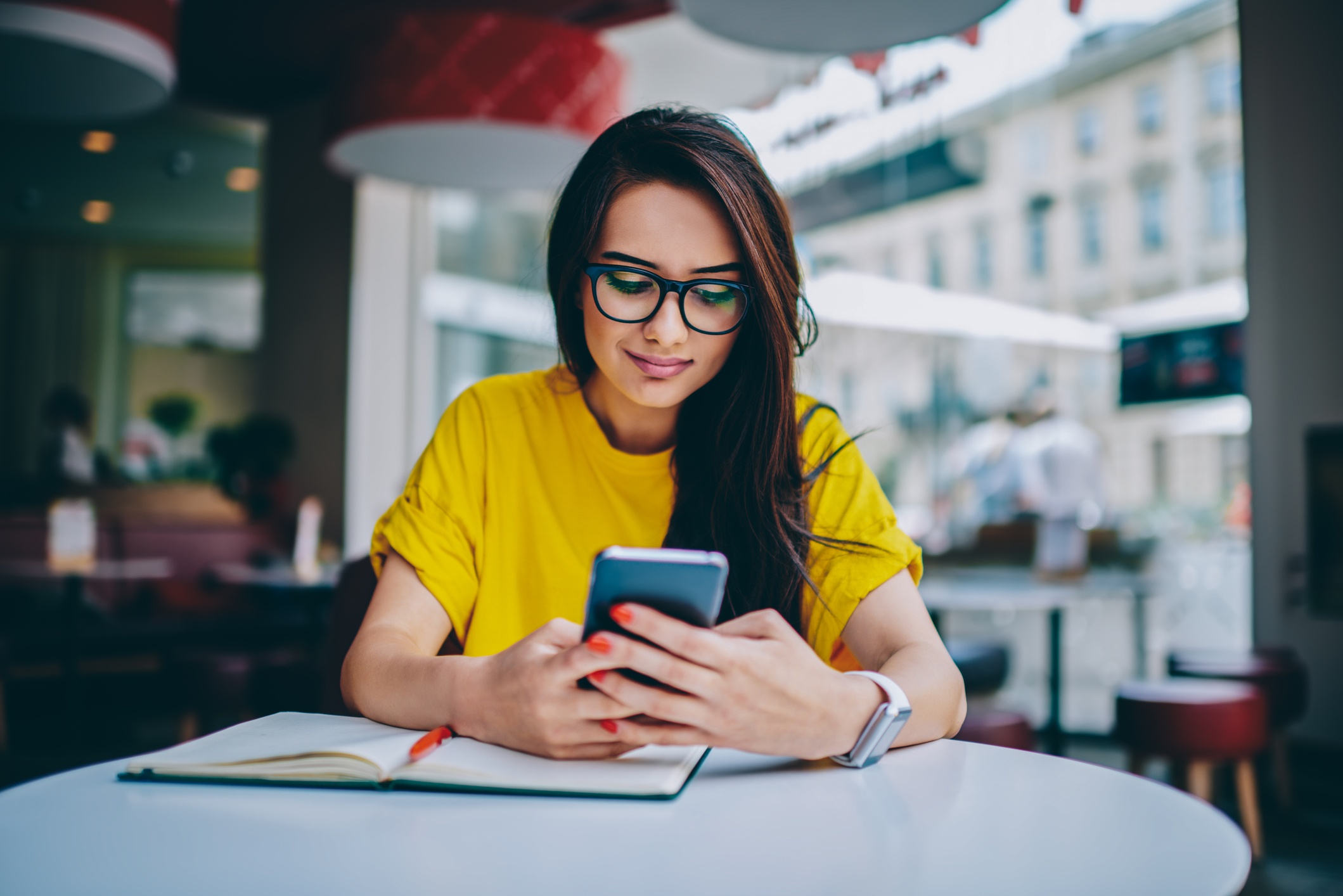 Woman in yellow shirt with glasses sitting at a table while looking at her phone