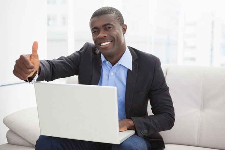 Man giving a thumbs up sitting on a white couch with a laptop