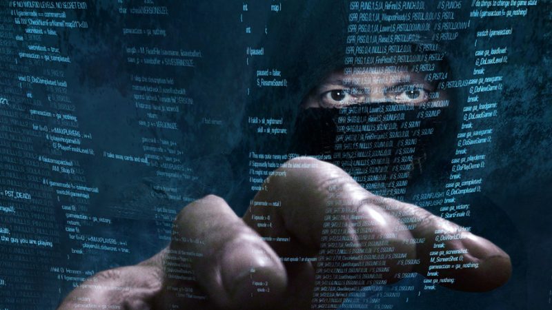 Hacker in mask reach hand out to steal data superimposed on screen